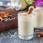 Horchata in two glasses next to cinnamon sticks, rice, and almonds.