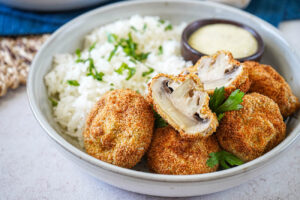 Rántott Gomba (Hungarian Fried Mushrooms) on a plate with rice, parsley, and tartar sauce.