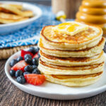 A stack of five Scotch Pancakes on a white plate with blueberries and strawberries.