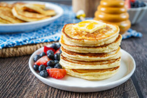 A stack of five Scotch Pancakes on a white plate with blueberries and strawberries.