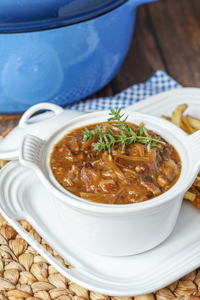 Carbonnade Flamande (Flemish Beef and Beer Stew) in a white bowl with a blue pot in the background.