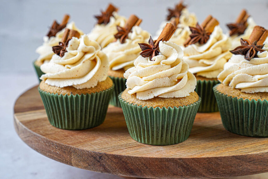Nine Chai Cupcakes with Brown Butter Frosting on a wooden board with cinnamon stick and star anise garnishes.