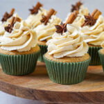 Nine Chai Cupcakes with Brown Butter Frosting on a wooden board with cinnamon stick and star anise garnish.