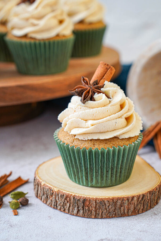 Side view of Chai Cupcakes with Brown Butter Frosting on a wooden coaster with more in the background on a wooden board.