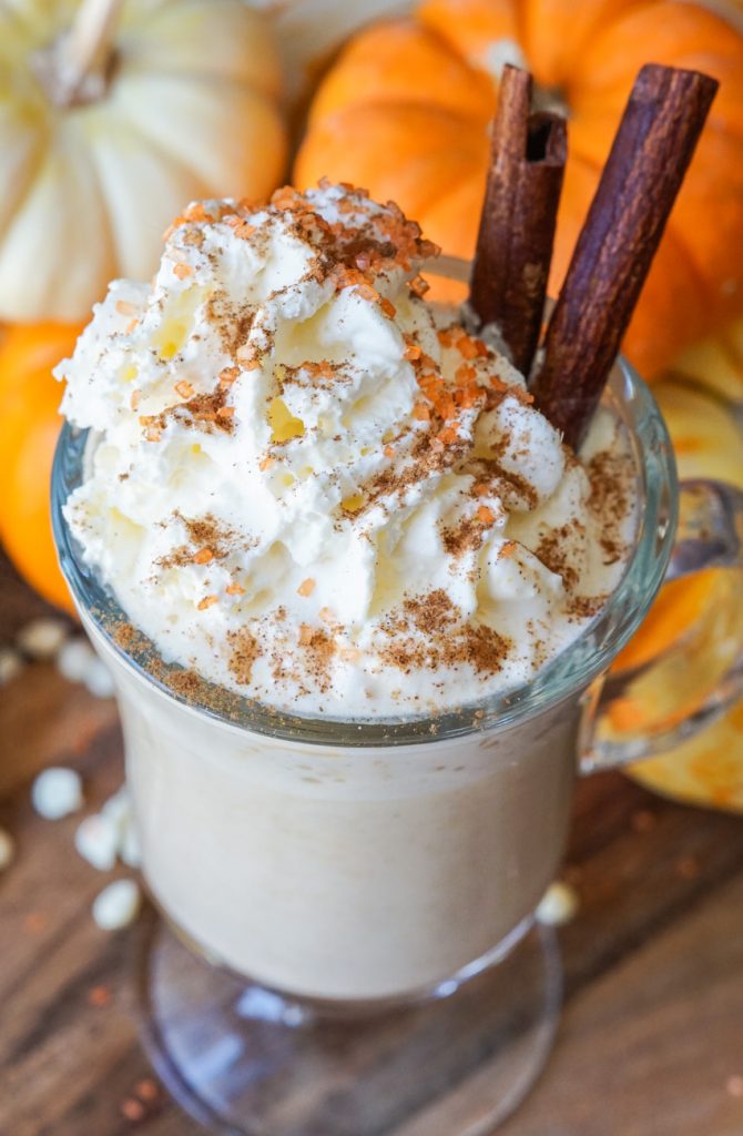 Close up of Pumpkin Spice White Hot Chocolate in a mug with whipped cream and cinnamon sticks.