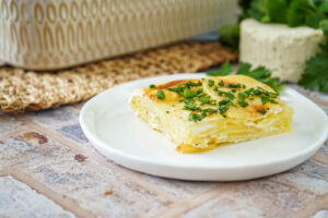 A slice of Garlic and Herb Potato Gratin on a white plate.