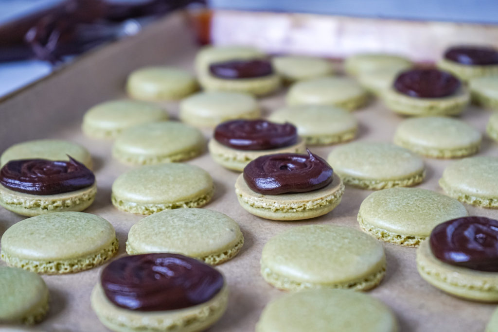 Piped ganache over Matcha Macarons on a baking sheet.