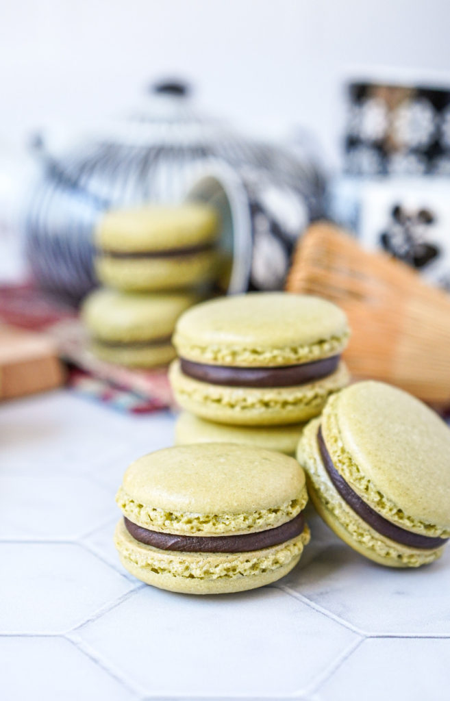 Side view of a stack of Matcha Macarons with Chocolate Ganache in front of a black and white tea set.