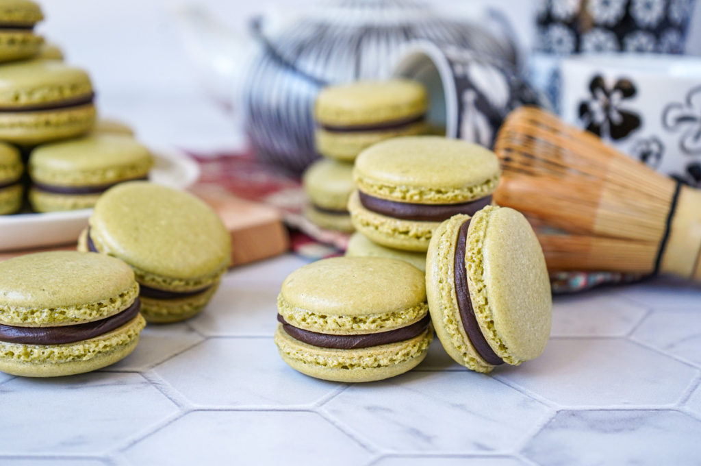 Stacks of Matcha Macarons with Chocolate Ganache in front of a black and white tea set.
