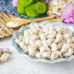 Sugar-Coated Cashew Nuts in a bowl next to flowers and two spoons.