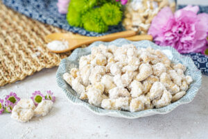 Sugar-Coated Cashew Nuts in a bowl next to flowers and two spoons.