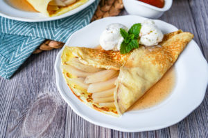 Champagne Poached Pear Crepes on a white plate with two scoops of ice cream.