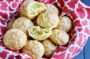 Gougères (French Cheese Puffs) in a red towel-lined basket with one cut in half to show airy center.