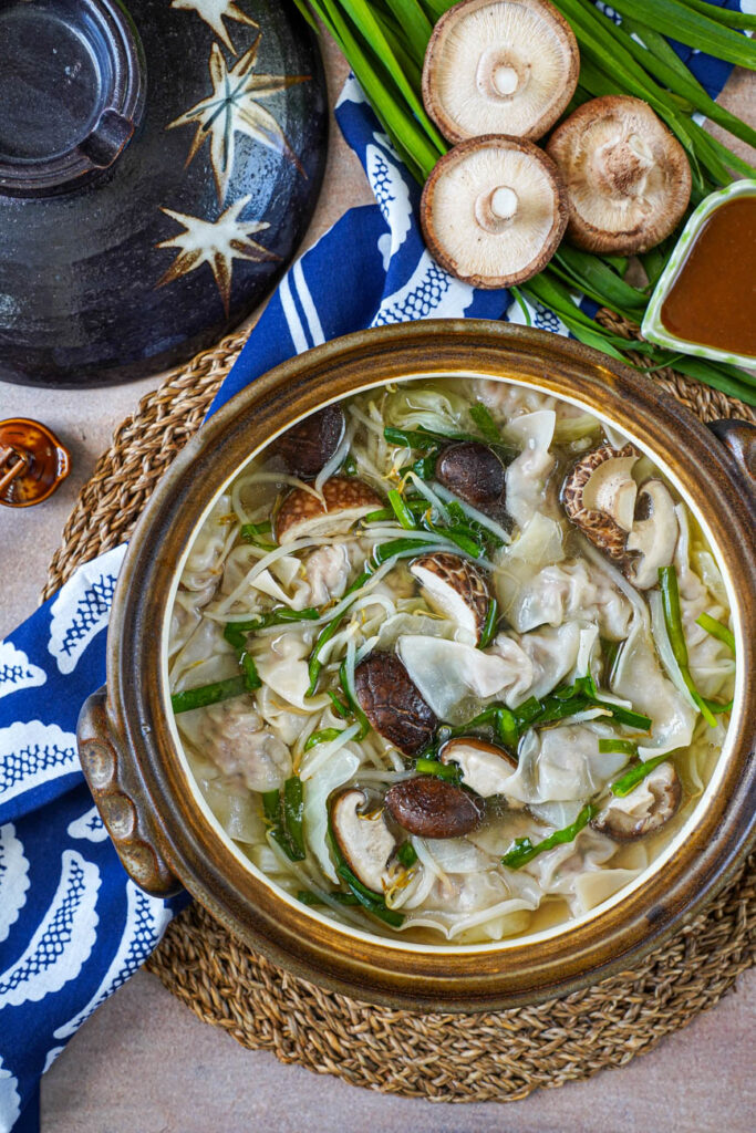 Aerial view of Gyoza Nabe (Japanese Dumpling Hot Pot) next to garlic chives, shiitake mushrooms, and miso dipping sauce.
