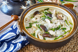 Gyoza Nabe (Japanese Dumpling Hot Pot) in a brown Donabe next to a blue gyoza towel.