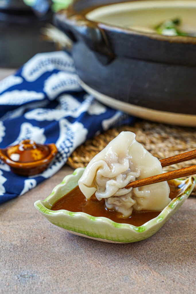Dipping a gyoza into the miso dipping sauce using chopsticks.