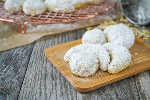 Round and crescent Kourambiethes (Greek Shortbread Cookies) on a wooden board.