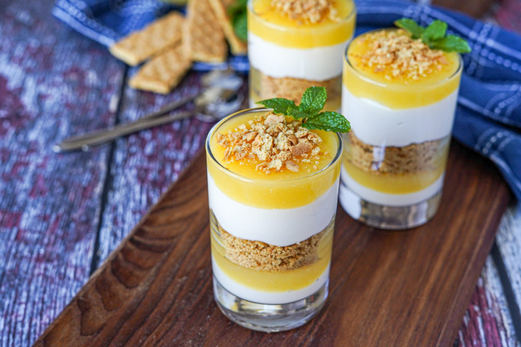 Meyer Lemon Parfaits in three clear glasses on a wooden board and topped with graham crackers and mint sprigs.