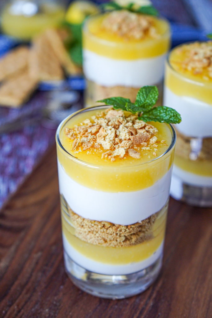 Close up of Meyer Lemon Parfaits in three clear glasses on a wooden board with graham crackers and mint.