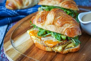 Croissant Breakfast Sandwich with egg, breakfast sausage, cheese, avocado, and arugula.