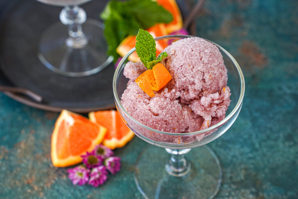 Close up of Sorbete de Vino Tinto (Red Wine Sorbet) in a glass with a mint sprig and orange peel.