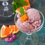 Sorbete de Vino Tinto (Red Wine Sorbet) in a glass next to orange wedges and purple flowers.