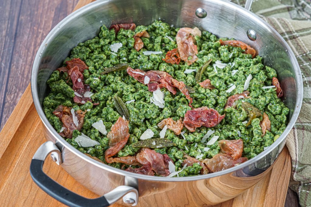 Spinach Spätzli with Sage and Speck in a steel pan resting on a wooden board.