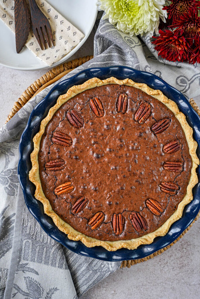 Aerial view of Brownie Pecan Pie in a blue pie dish next to red and white flowers.