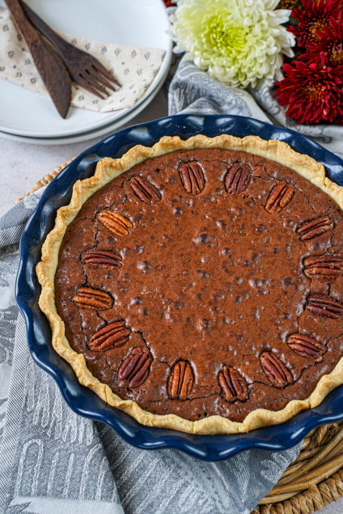 Close up of Brownie Pecan Pie with red and white flowers and plates in the background.