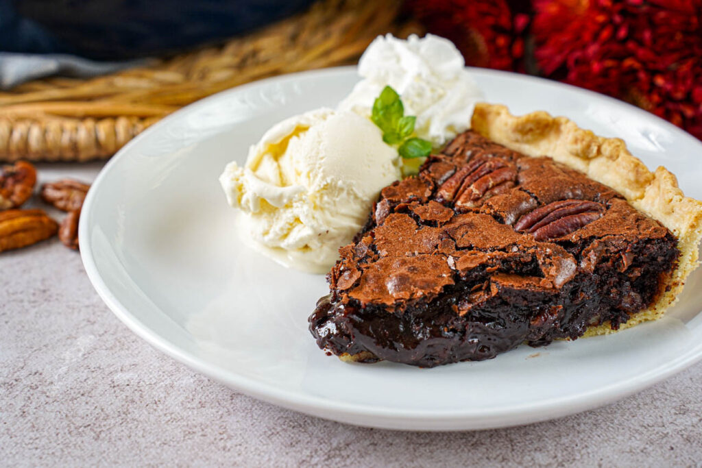 A slice of Brownie Pecan Pie on a plate with vanilla ice cream and whipped cream.