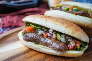 Two Choripán (Argentinian Chorizo Sandwiches) on a wooden board.