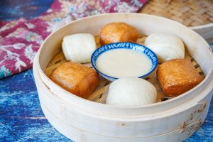Gold and Silver Mantou in a bamboo basket with a bowl of condensed milk.