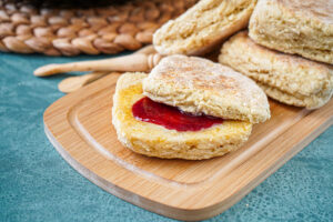 Four Irish Soda Farls on a wooden board with one cut in half and filled with butter and raspberry jam.
