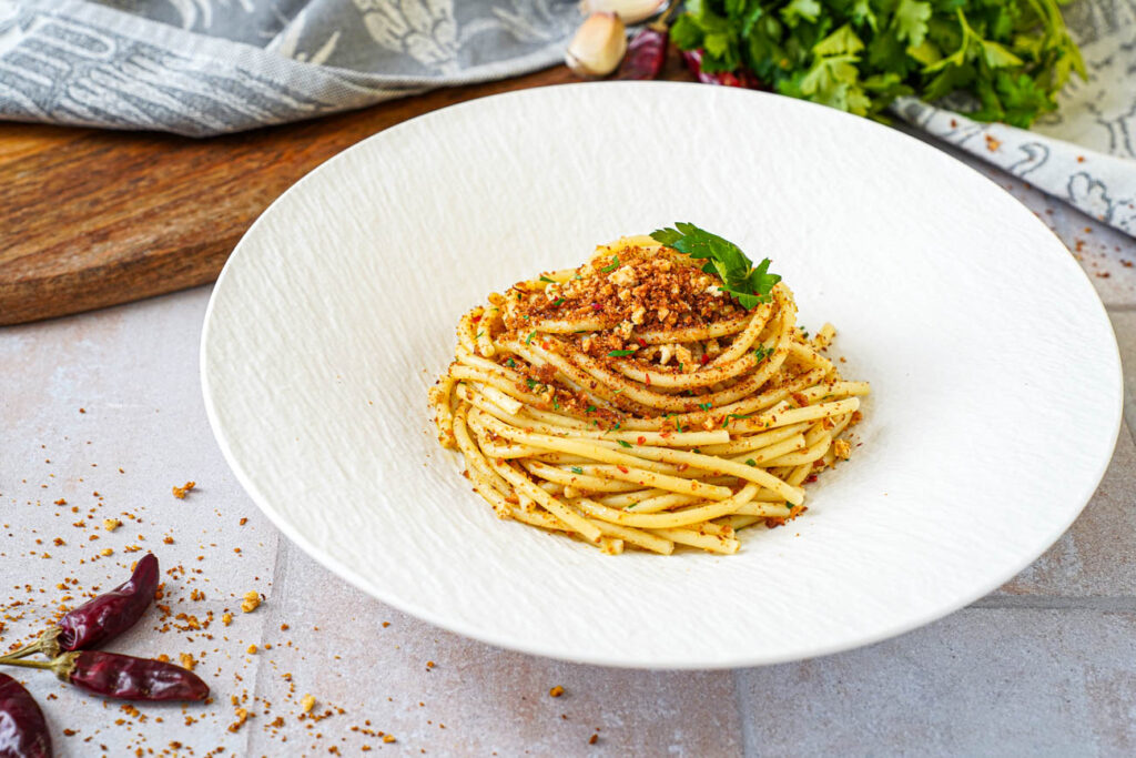 Pasta con la Mollica (Pasta with Breadcrumbs) in a white bowl with parsley sprigs.