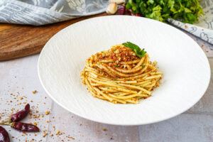 Pasta con la Mollica (Pasta with Breadcrumbs) in a large white bowl with parsley sprigs.