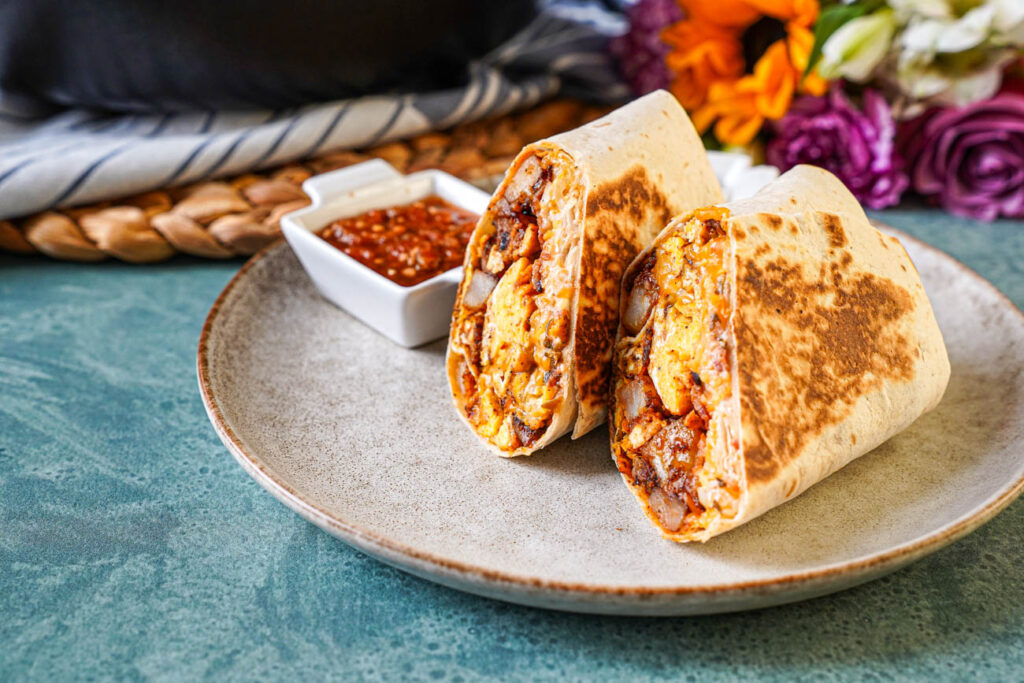 Bacon Breakfast Burritos on a plate with salsa and flowers in the background.