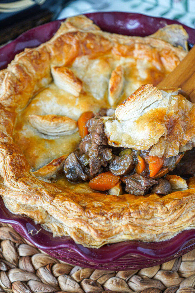 Beef and Mushroom Pie with Guinness in a pie dish with puff pastry and a spoon lifting up the meat filling.