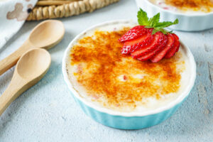 Strawberry Vanilla Yogurt Brûlée in a blue ramekin with a fresh strawberry and mint sprig on top.
