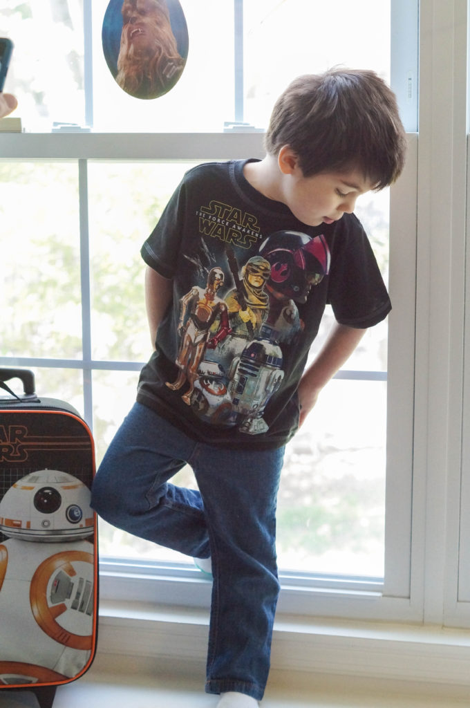 Boy standing in front of window next to BB8 suitcase.