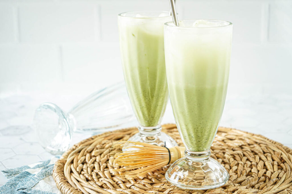 Matcha Egg Cream in two tall glasses with a third glass on its side in the background.
