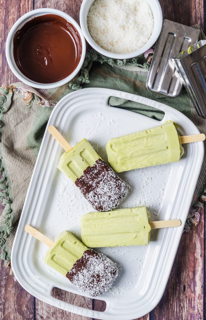 Aerial view of Paletas de Aguacate y Coco (Mexican Avocado and Coconut Popsicles) on a platter next to chocolate and coconut.