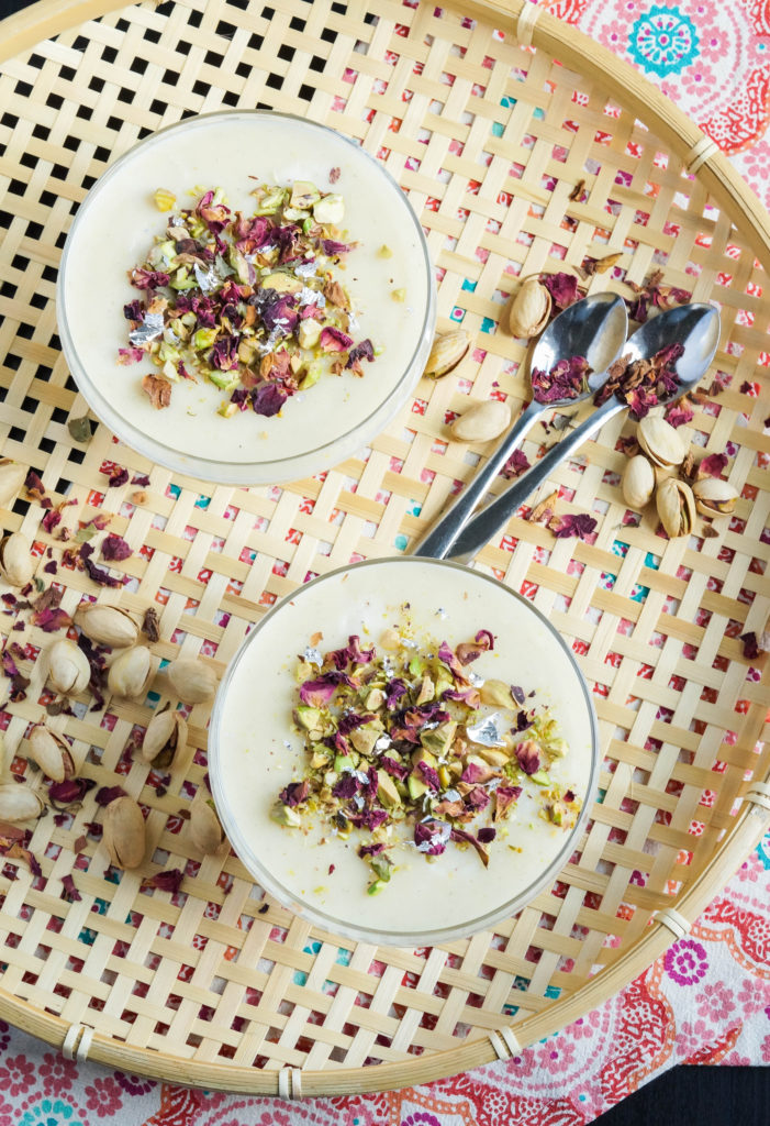 Aerial view of Nani's Firni (Pakistani Screwpine-Infused Ground Rice Pudding) in two glass bowls with scattered pistachios and roses.