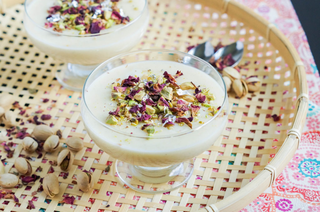 Nani's Firni (Pakistani Screwpine-Infused Ground Rice Pudding) in two glass bowls and topped with rose petals, pistachios, and silver.