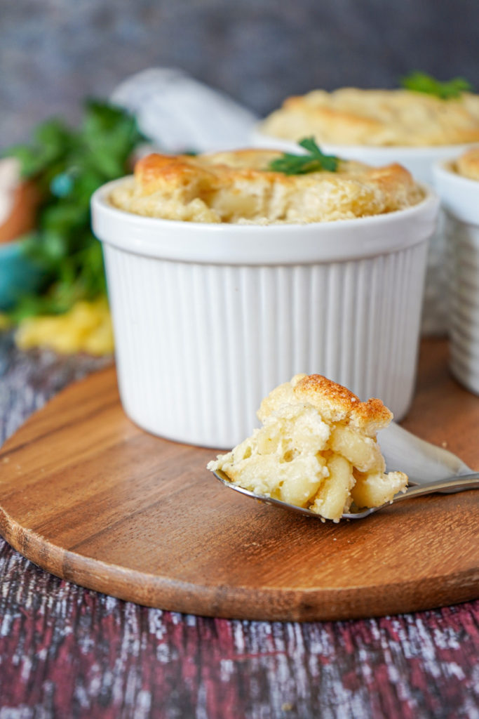 Spoonful of Macaroni and Cheese Soufflé in front of three white ramekins.