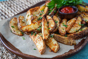 Parmesan Potato Wedges on a parchment lined wooden board with ketchup and parsley.