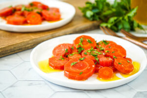 Zanahorias Aliñadas (Spanish Marinated Carrots) on two white plates with parsley in the background.