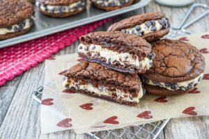 Brownie Cookie Dough Sandwich Cookies on a parchment-lined wire rack with one cut in half.