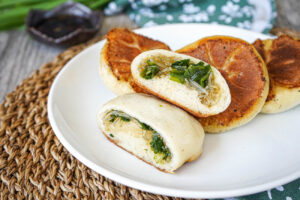 Jiu Cai Shui Jian Bao (Taiwanese Pan-Fried Chive Buns) on a white plate with one cut in half to show filling.