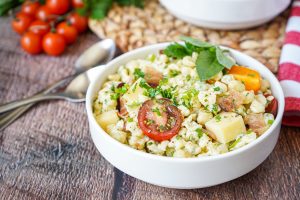 Spätzlesalat (German Spaetzle Pasta Salad) in a white bowl next to two spoons.