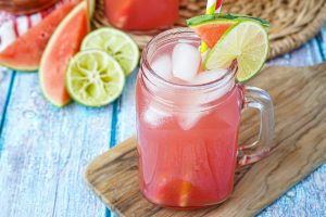 Agua de Sandía (Mexican Watermelon Water) in a glass mug with lime and watermelon in the background.
